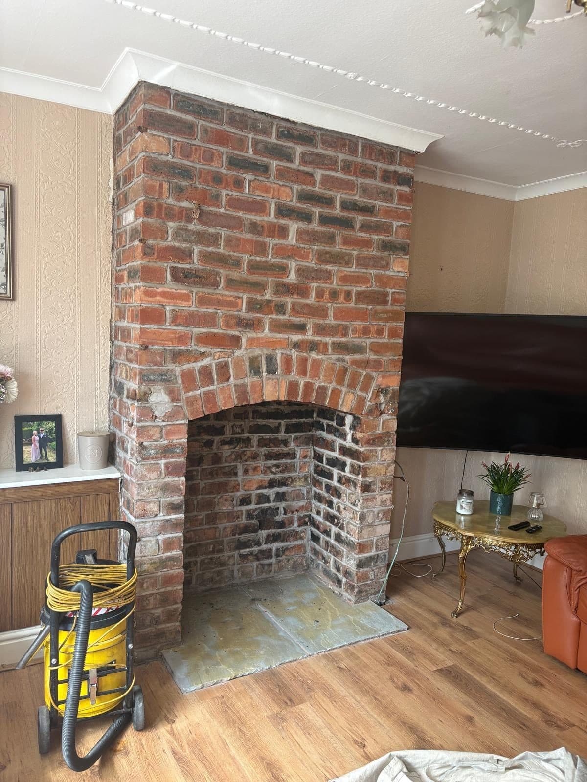 Exposed brick chimney breast with an arched opening, install in progress, vacuum and dust sheet still in the room