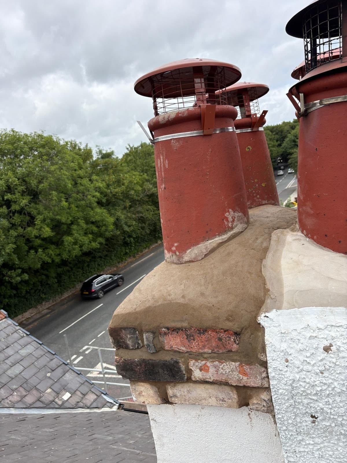 Chimney stack with newly formed mortar flaunching and three red clay pots fitted with cowls, rooftops and road below