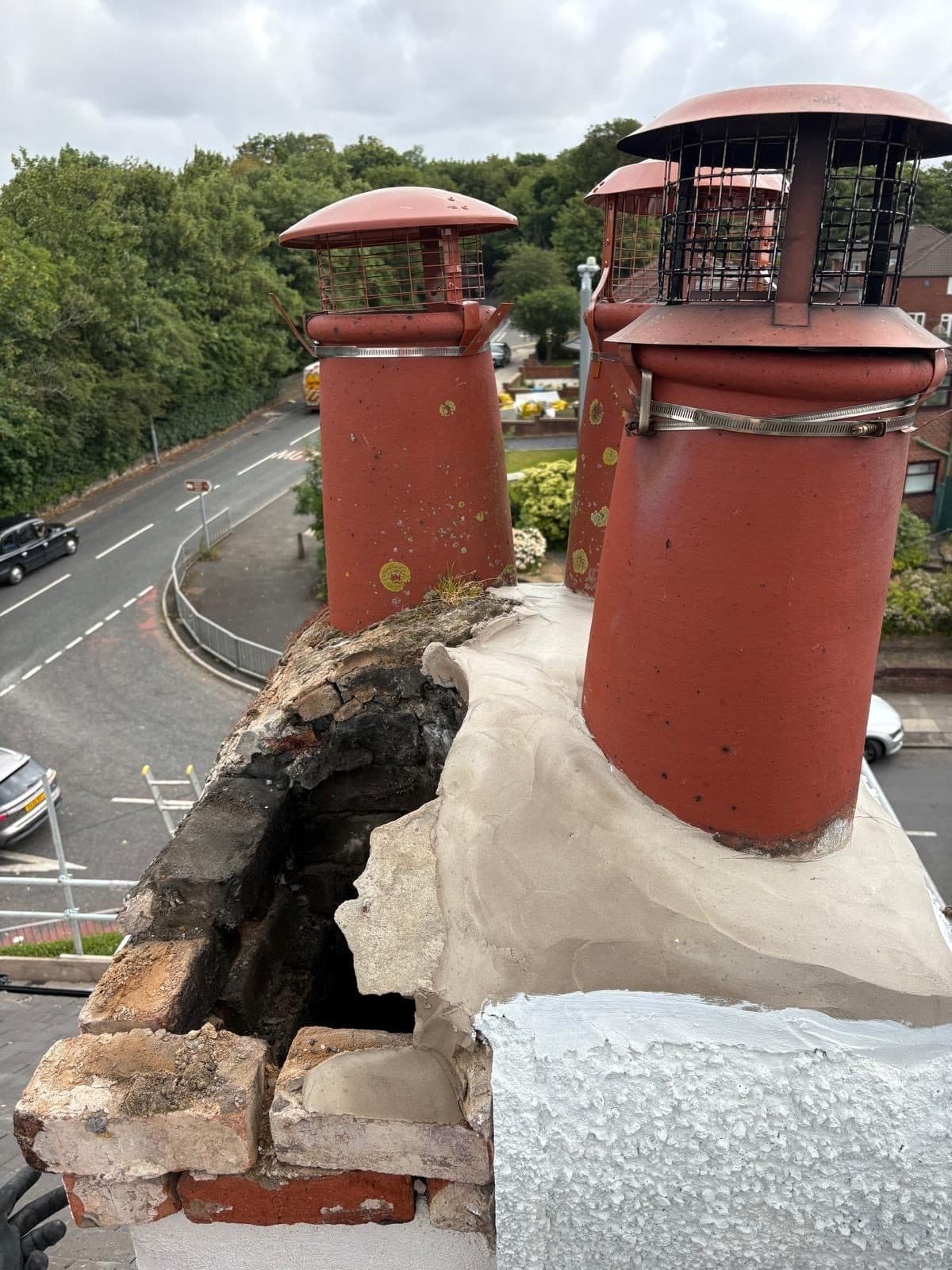 Chimney stack with the mortar flaunching cracked and broken away, exposing a dark void and saturated brickwork beneath the pots
