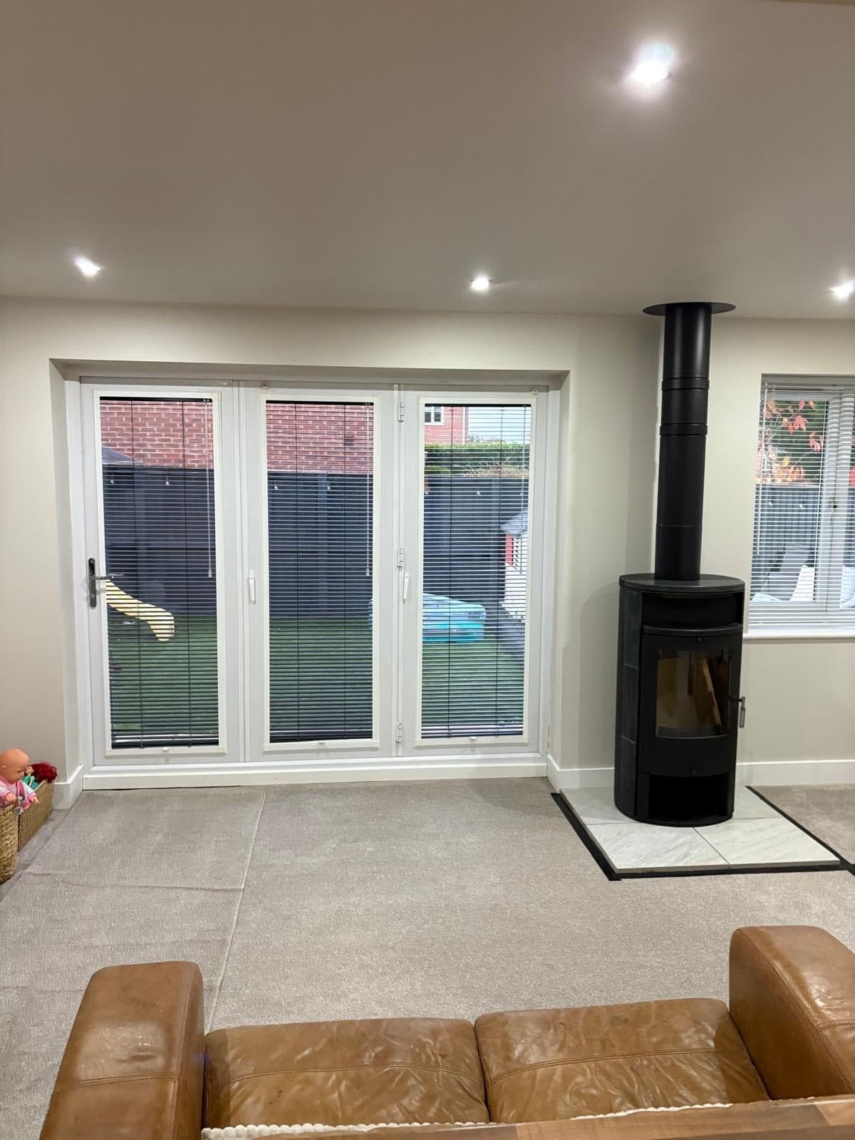 The same lounge finished and furnished, black cylindrical stove on a hearth pad with tan leather sofas in the foreground