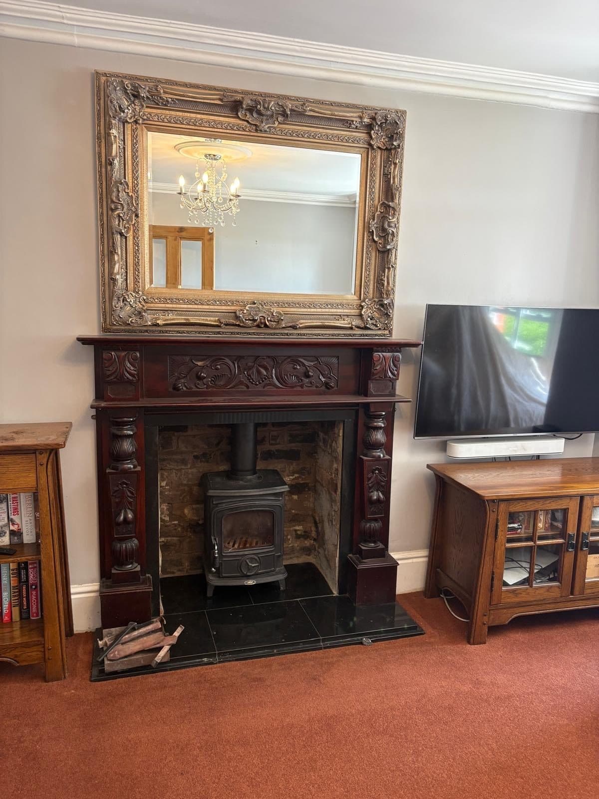 Small stove set into an ornate carved dark wood fireplace surround with a gilt overmantel mirror