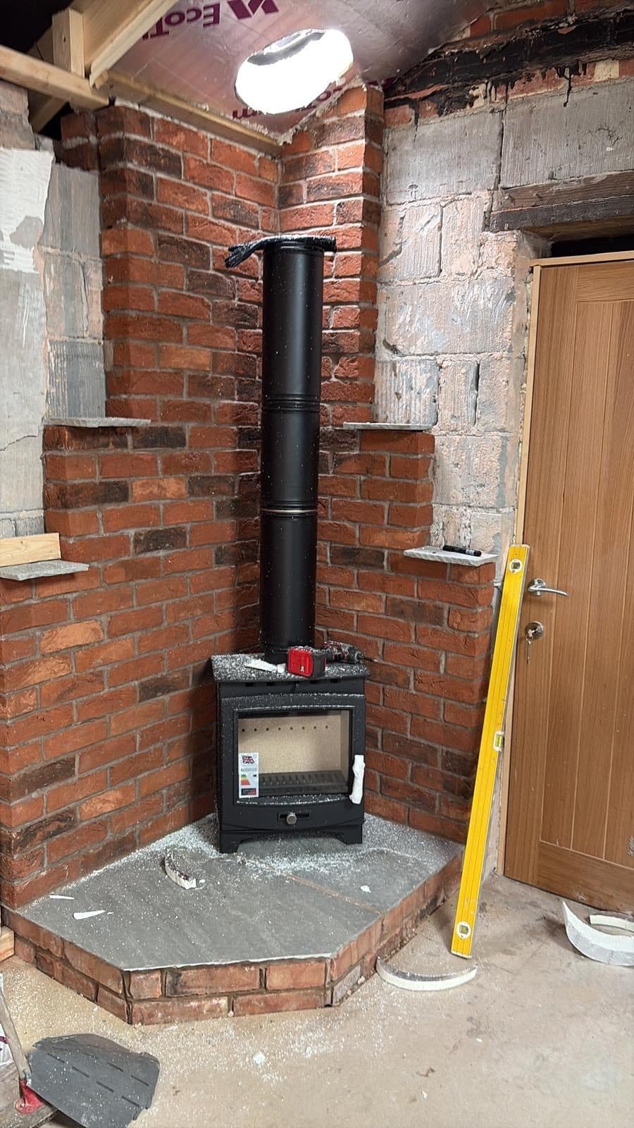 Small stove on a slate hearth in a brick outbuilding with an internal twin-wall flue, spirit level propped against the wall
